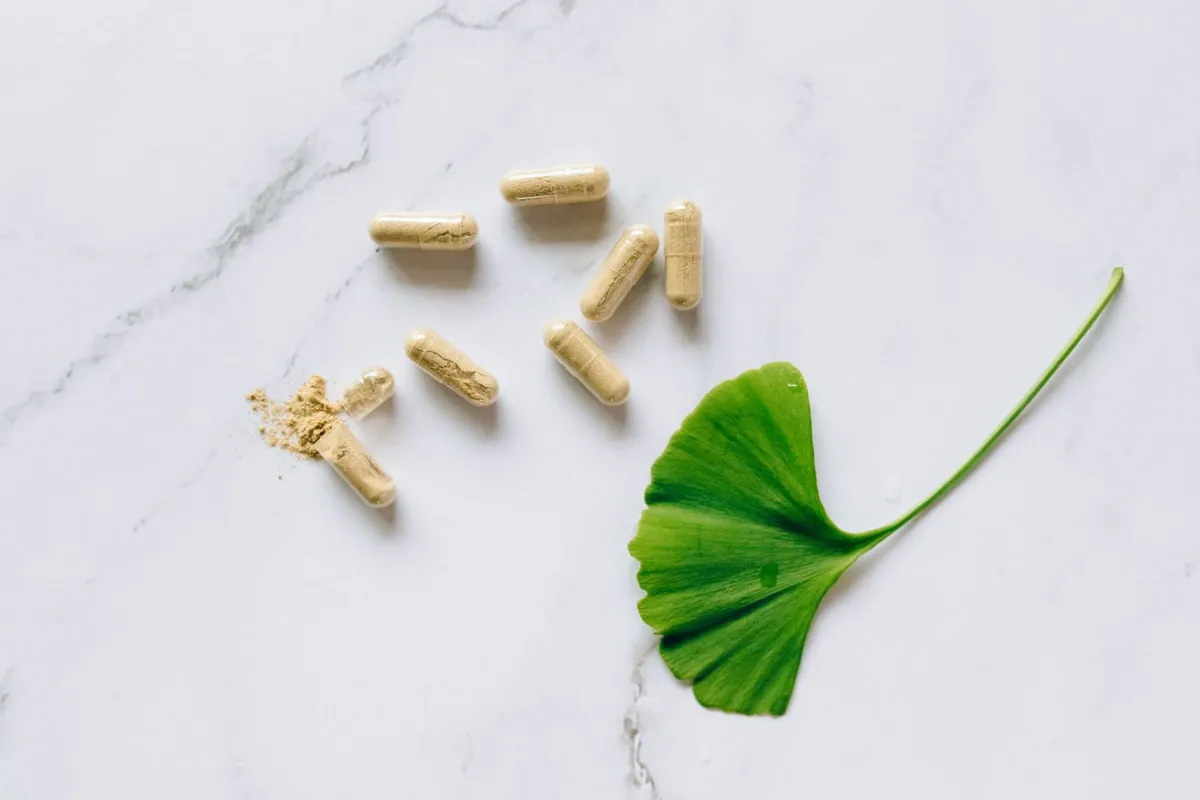Herbal supplement capsules arranged next to a green leaf on a marble surface, seen from above