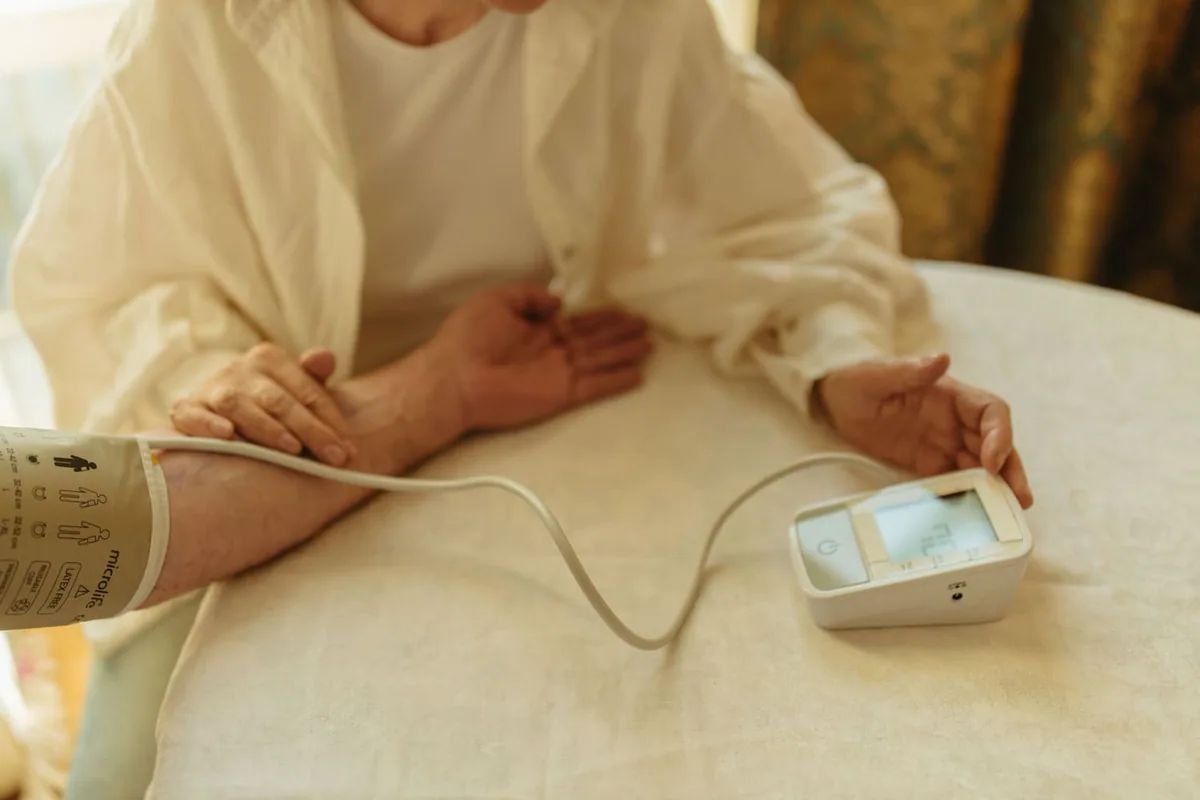 A person checking their blood pressure at home with a digital monitor in warm low light