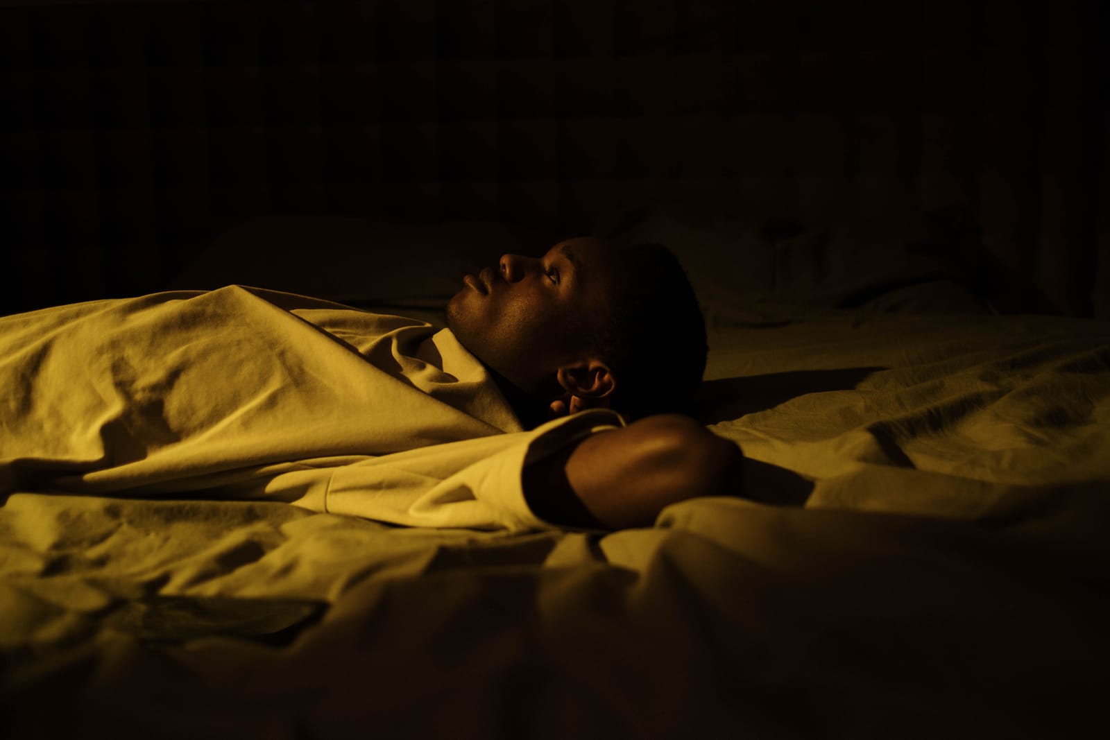 A man lying awake in a dark bedroom at night, staring upward, unable to sleep