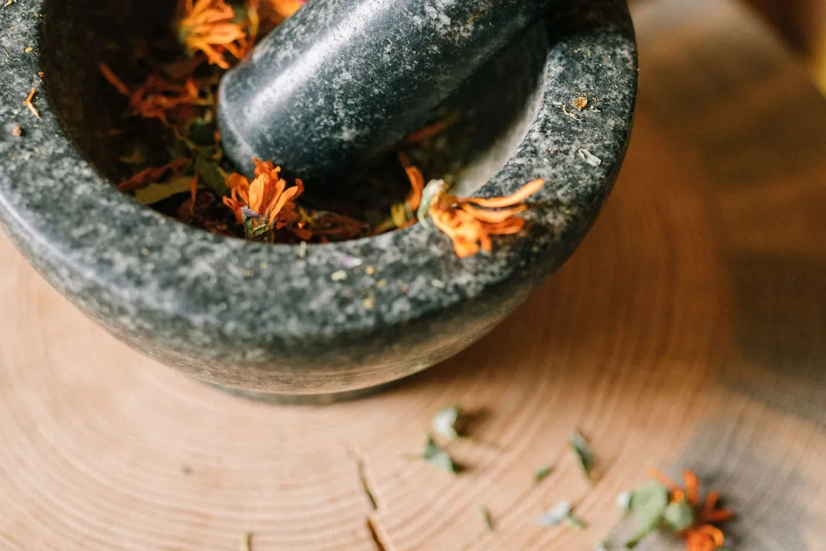 Dried herbs ground in a granite mortar and pestle on a rustic wooden board