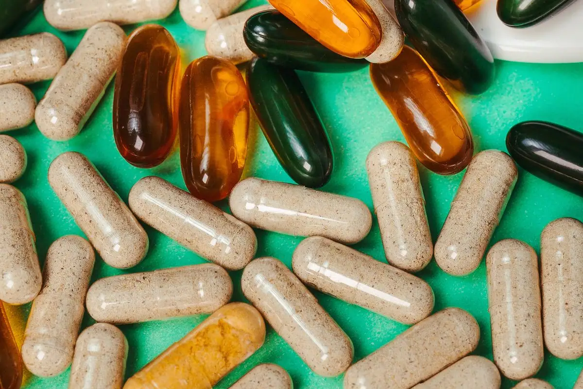An assortment of supplement capsules and tablets scattered on a bright green surface