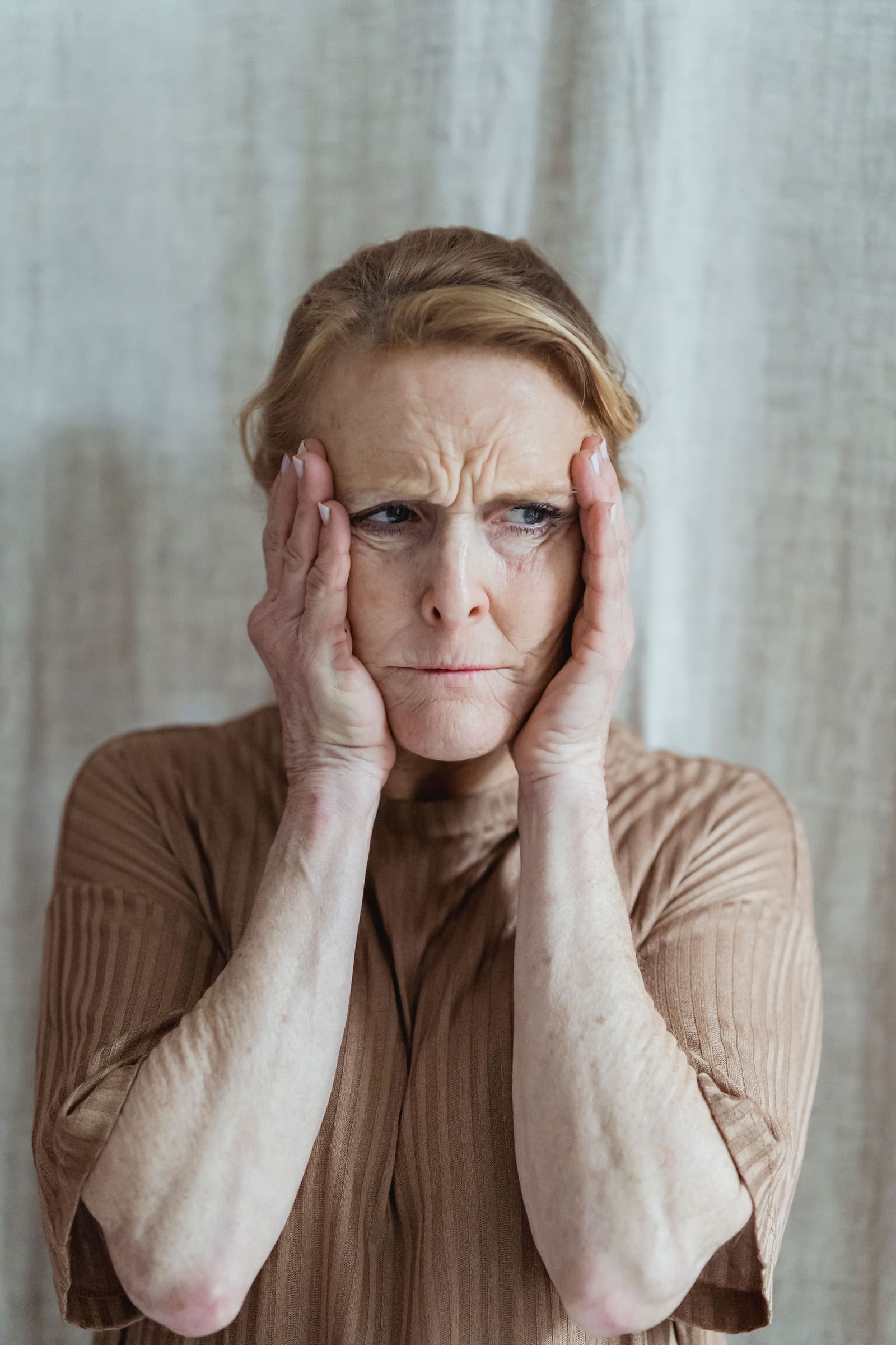 A woman with a concerned expression holding her face, representing the subtle discomfort that can accompany elevated blood pressure