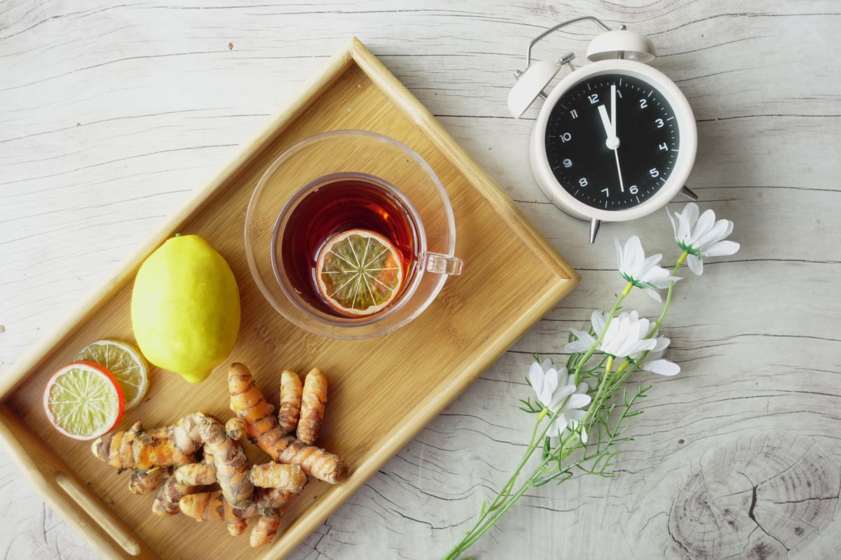 A tray of herbal tea with lemon, turmeric root, and fresh flowers representing multiple wellness ingredients