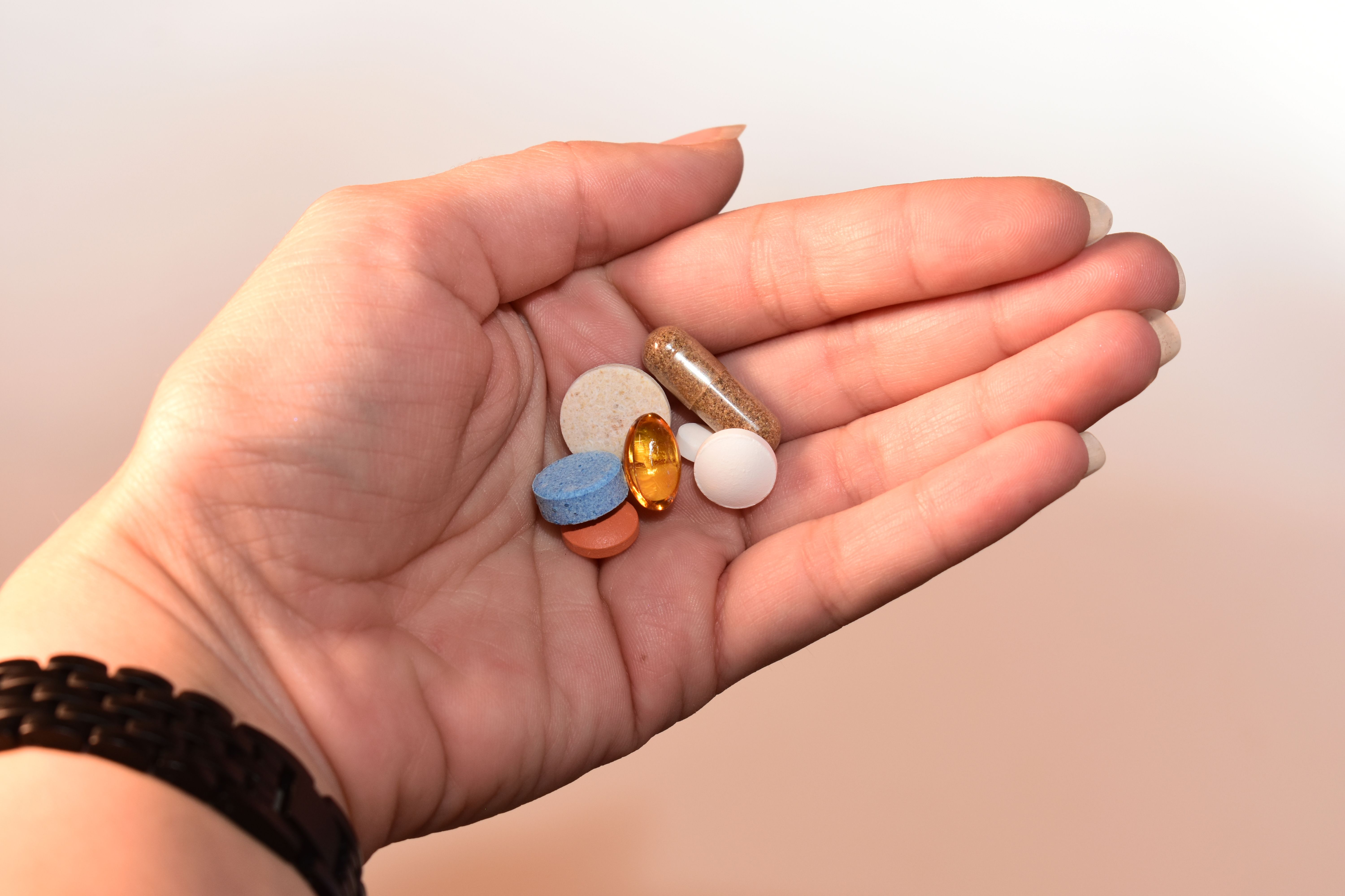 A hand holding an assortment of loose pills and capsules, representing the mix of supplements people take without checking for blood pressure interactions