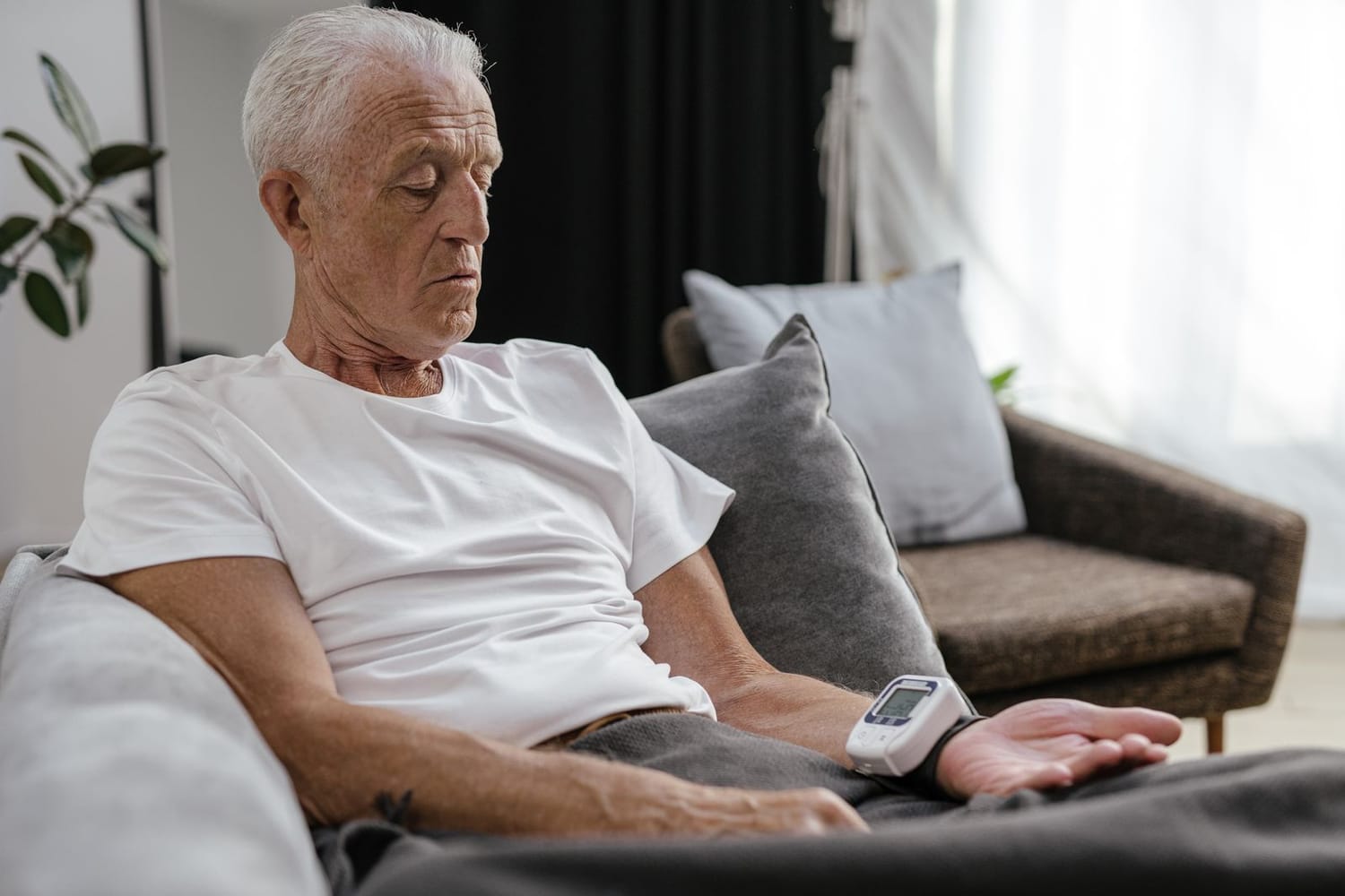 An older man sitting calmly on a sofa in the evening, checking his blood pressure with a wrist monitor at home